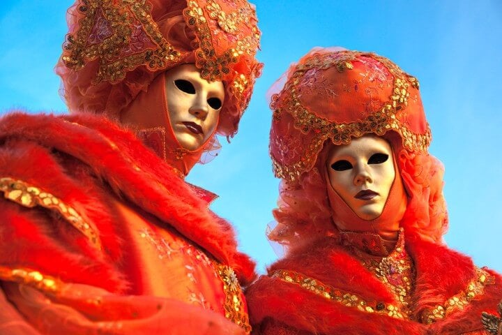 Dos personas disfrazadas con máscaras y trajes naranja en el carnaval de Venecia