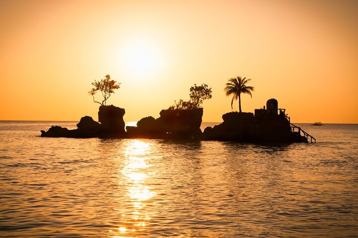 Vista al atardecer de dos peñones con palmeras desde la Isla de Boracay, Filipinas