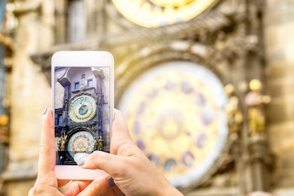 Un móvil saca una foto del reloj de Praga, en primer plano se ve el móvil, al fondo el reloj
