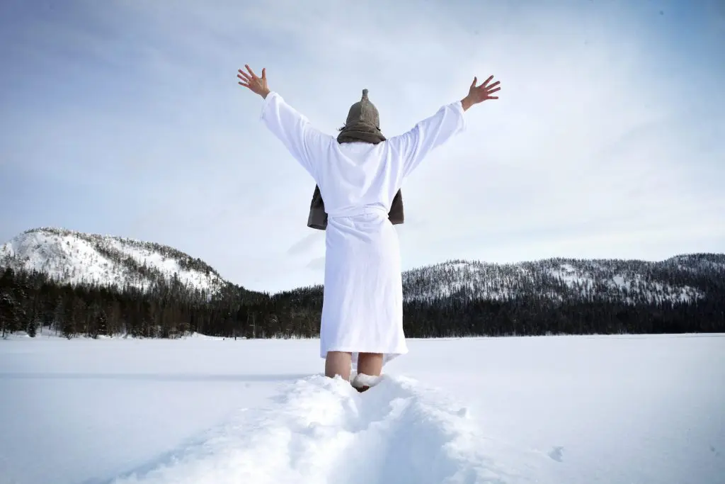 Mujer andando en albornoz por la nieve tras salir de la sauna en la Laponia finlandesa