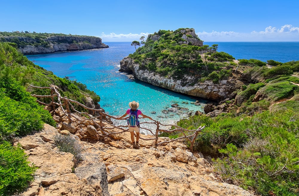 Turista con sombrero y mochila en el acantilado cerca del Caló des Moro, Mallorca