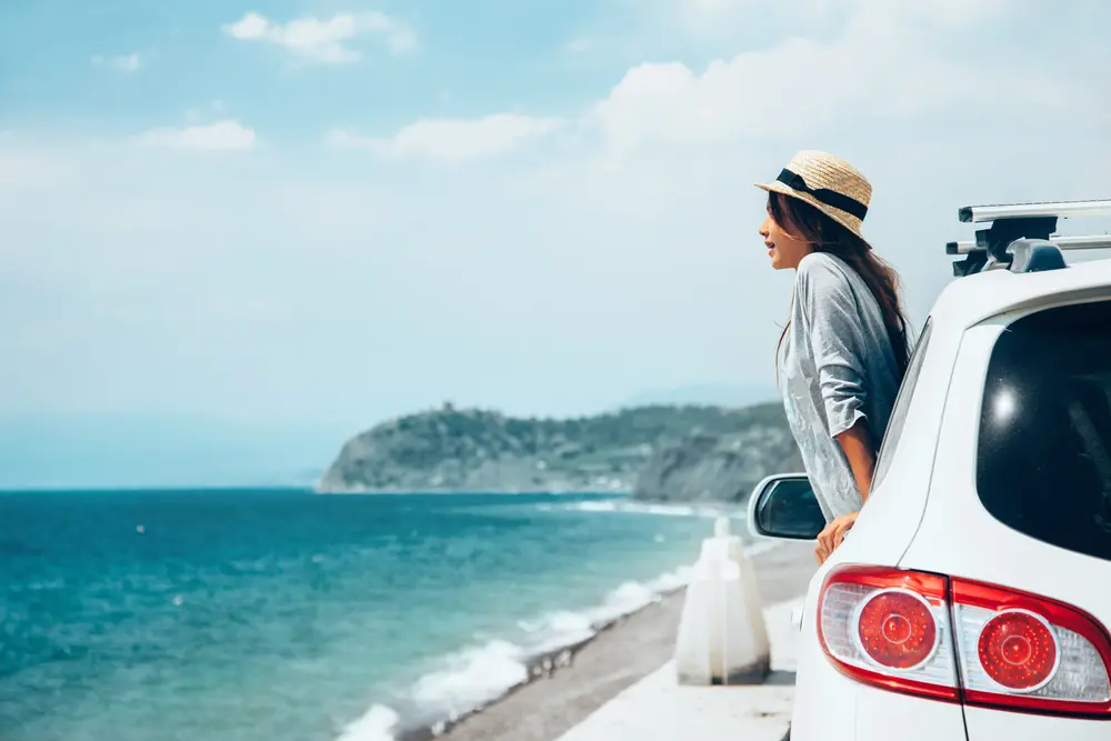 mujer en coche con vistas al mar en viaje de verano a la playa en menorca