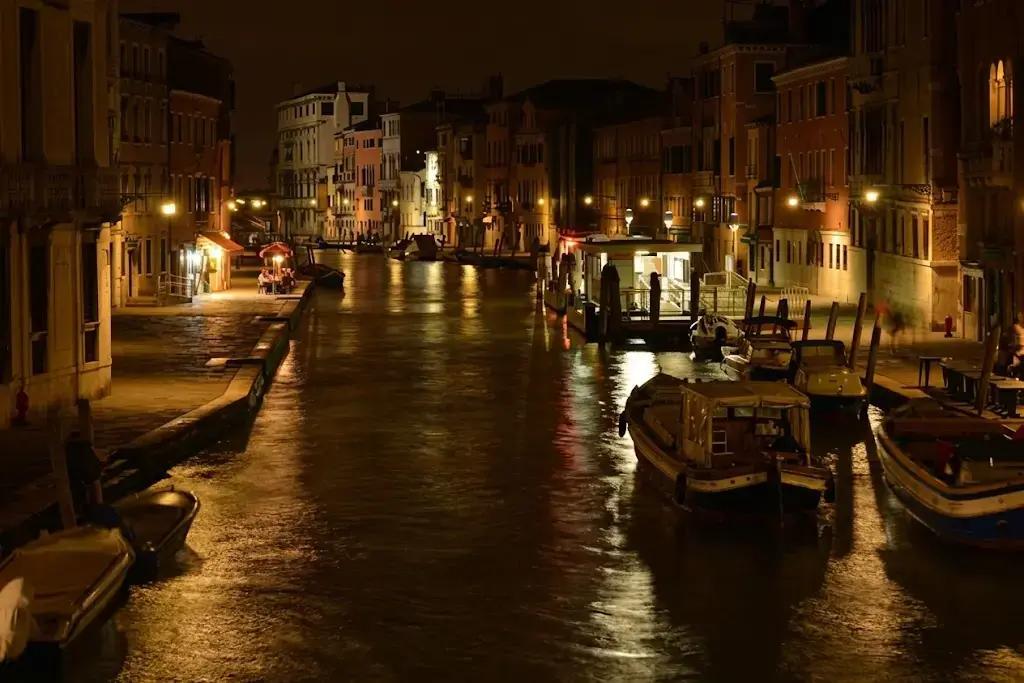Canal de Venecia de noche iluminado por farolas reflejadas en el agua oscura